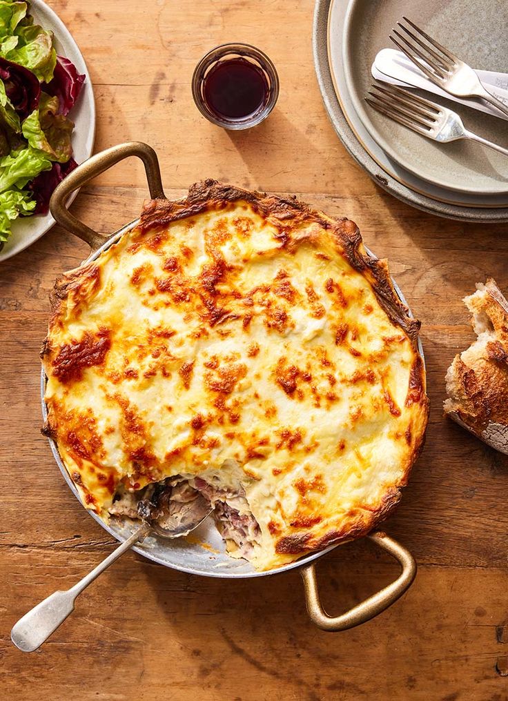 a casserole dish on a wooden table with plates and utensils next to it