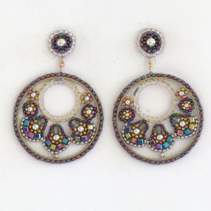 a pair of earrings with beading and glass beads on the bottom, sitting on a white surface