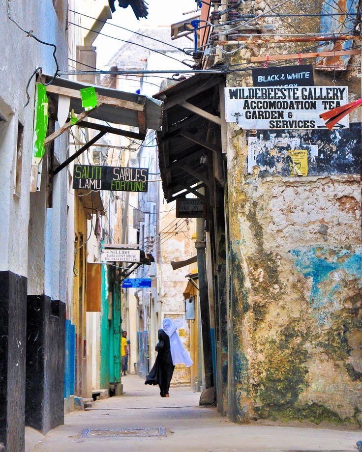 a woman walking down a street next to a tall building with signs on the side of it