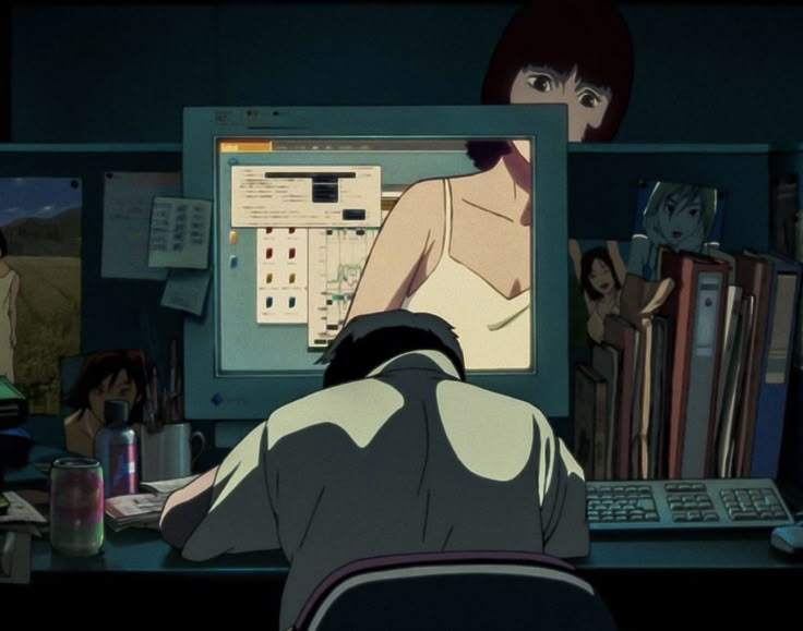 a person sitting at a desk in front of a computer monitor with an anime character on it