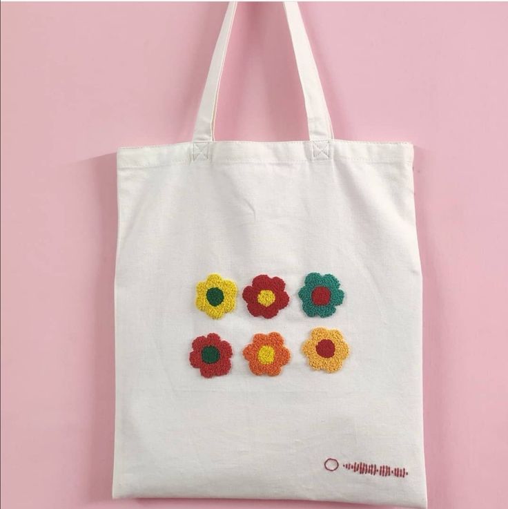 a white tote bag with flowers embroidered on the front and sides, hanging from a hook