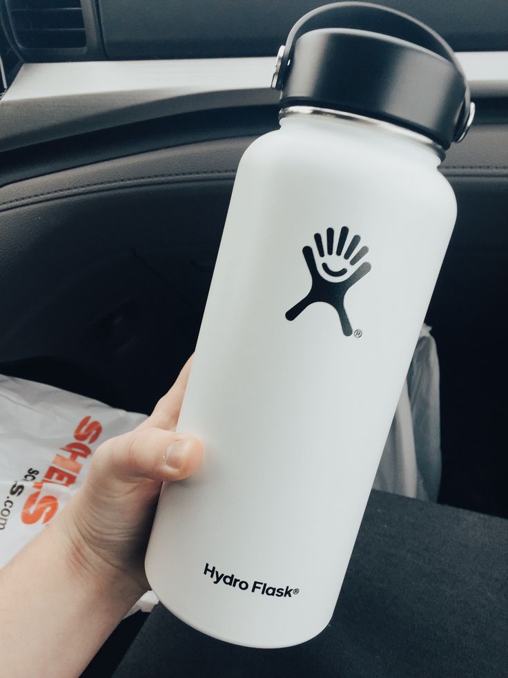 a hand holding a white hydro flask in the back seat of a car,