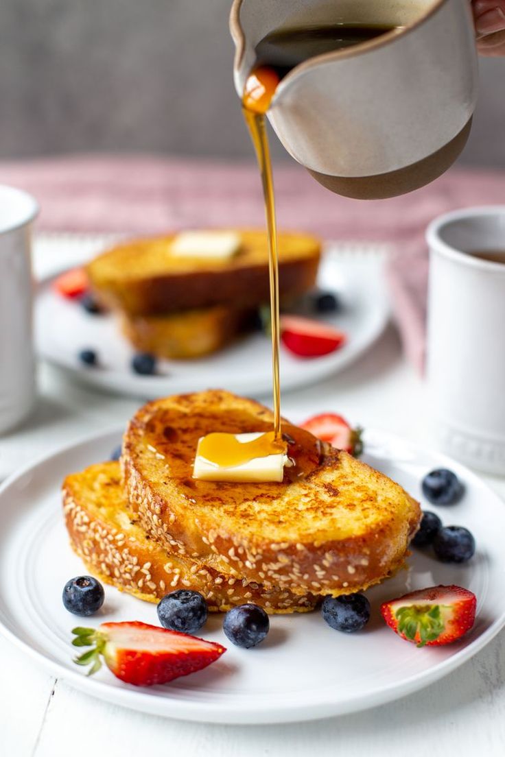 french toast with butter and blueberries on a white plate, being drizzled with syrup