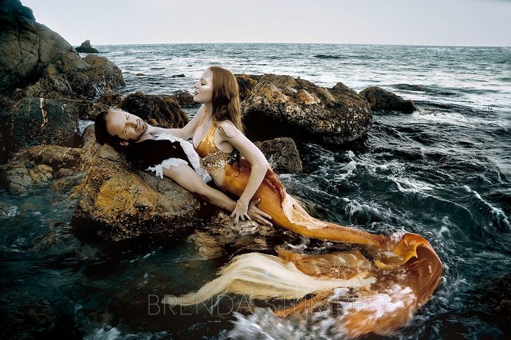 two women laying on rocks in the ocean with their arms around each other and looking up at the sky