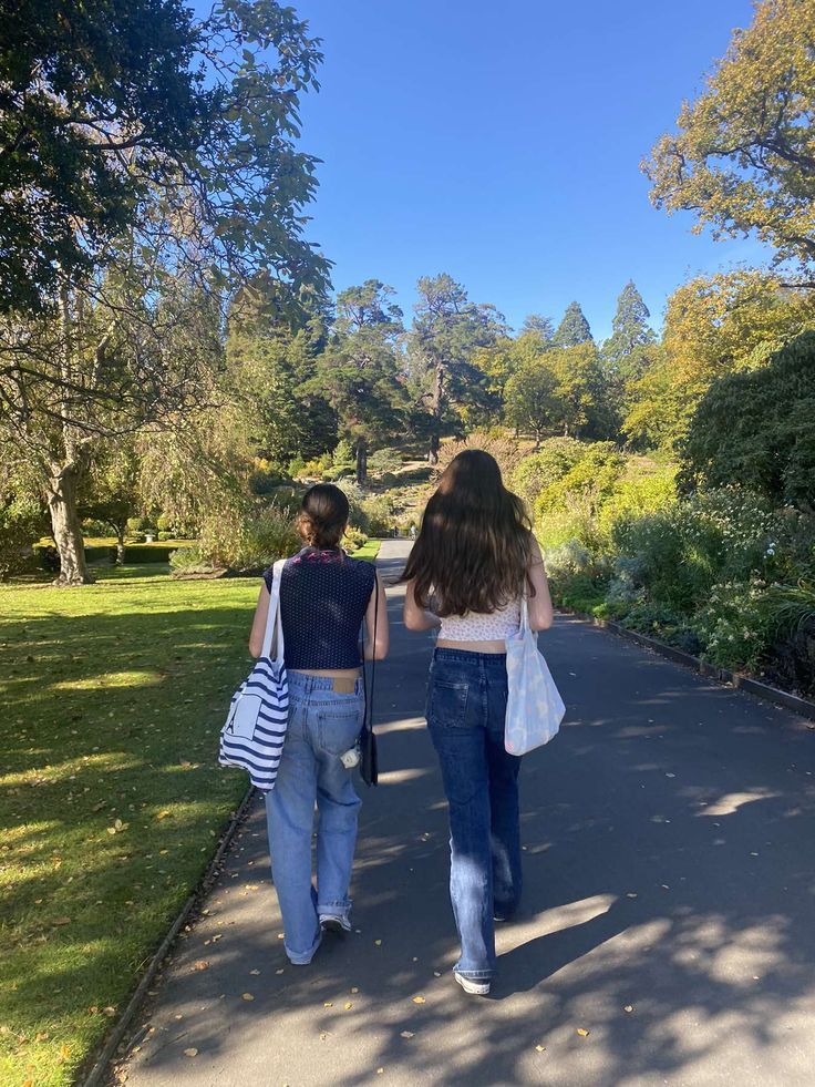 two women walking down a path in the park with their back to the camera and holding hands