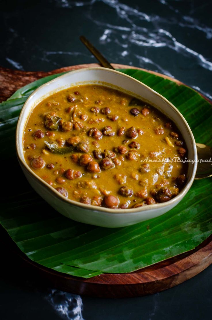 a white bowl filled with beans on top of a green leafy plate next to a spoon