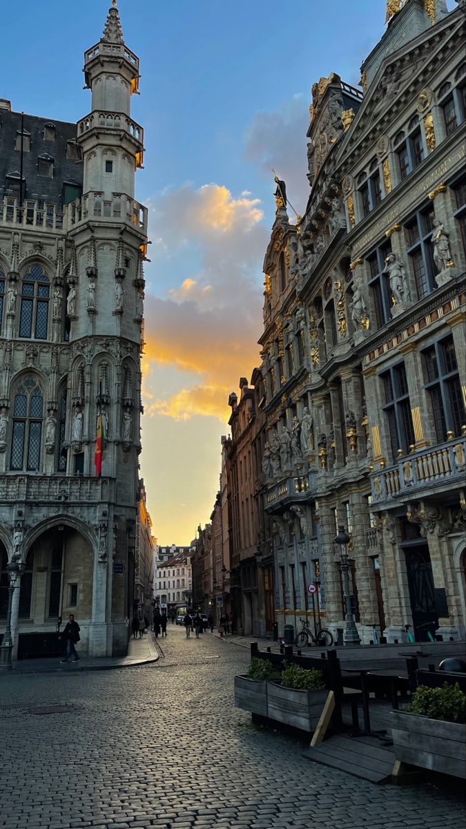 an old city street with buildings and people walking on the sidewalks at sunset or dawn