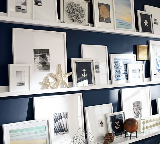 a wall filled with lots of framed pictures and art on top of white shelving