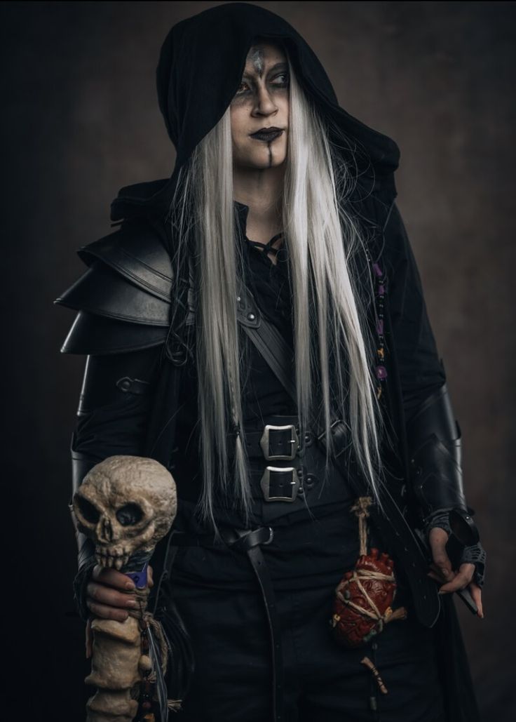 a man with long white hair wearing black clothing and holding a skull in his hand