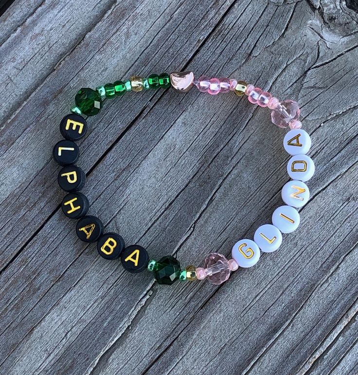 a beaded bracelet with beads and letters on it sitting on a piece of wood