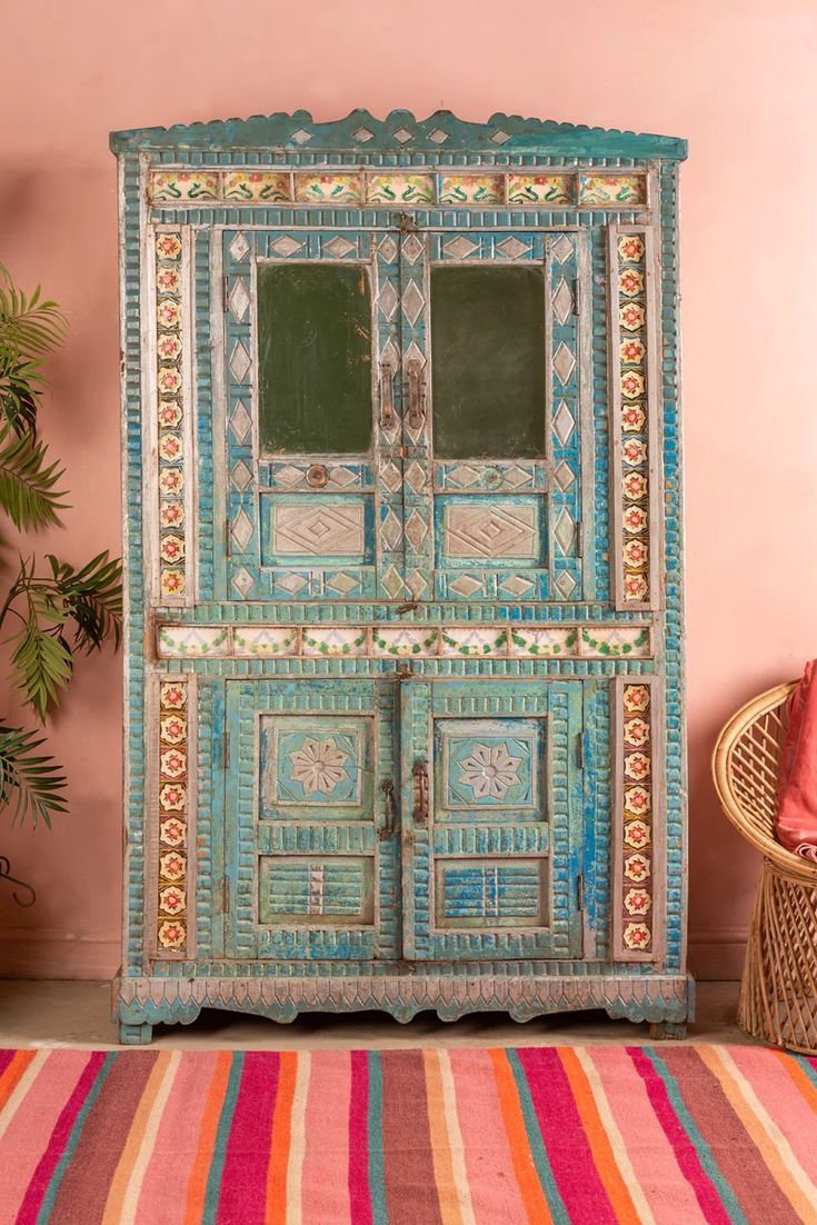 an old wooden cabinet painted in blue and pink with colorful stripes on the floor next to a potted plant