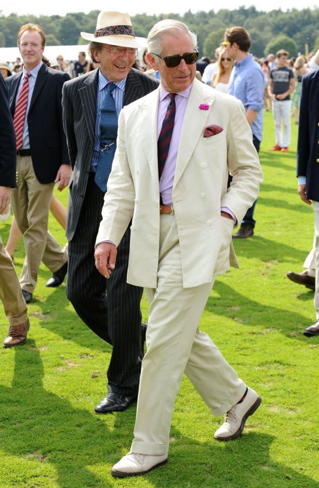 two men in suits and ties are walking on the grass with other people behind them