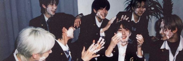 a group of young men standing next to each other in front of a wall with their hands up