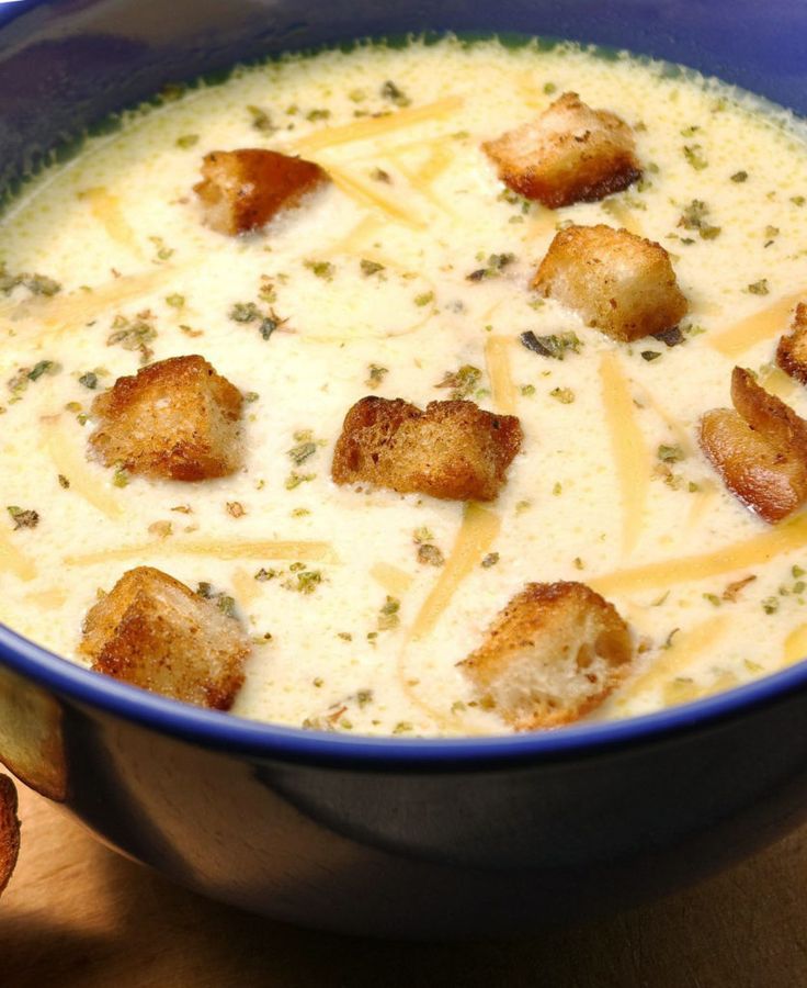 a blue bowl filled with soup and croutons on top of a wooden table