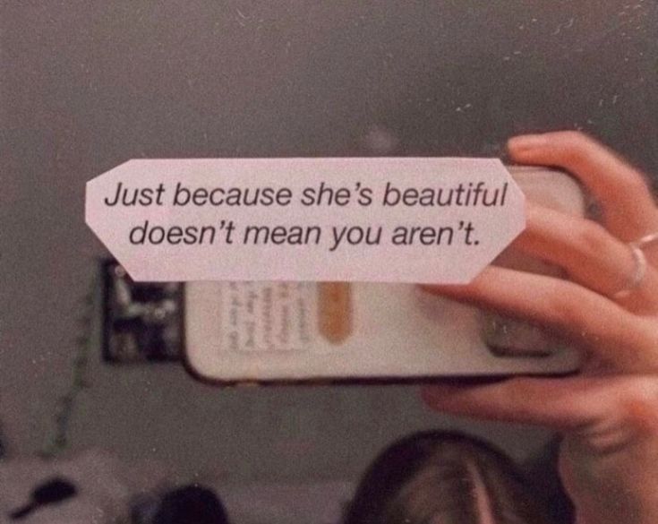 a woman taking a selfie with her cell phone while holding up a sign that says just because she's beautiful, doesn't mean you aren't