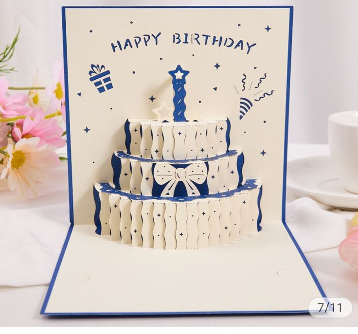 a birthday card with a three tier cake on it's side and flowers in the background