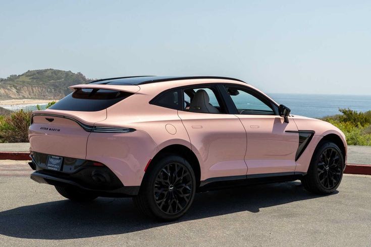 a pink sports utility vehicle parked on the side of the road near the ocean and hills