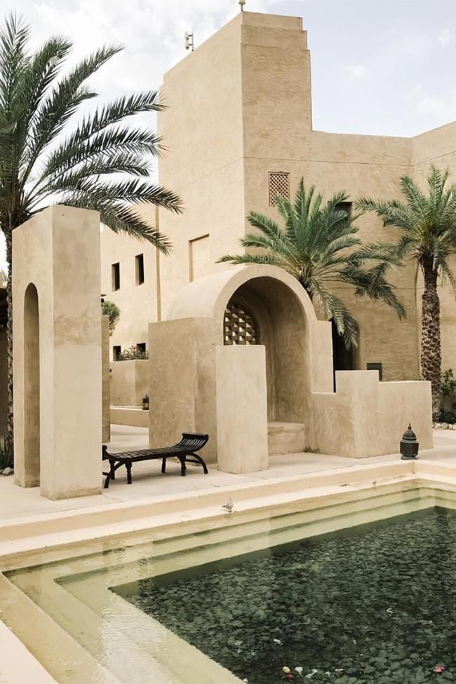 an outdoor swimming pool in front of a large beige building with palm trees around it