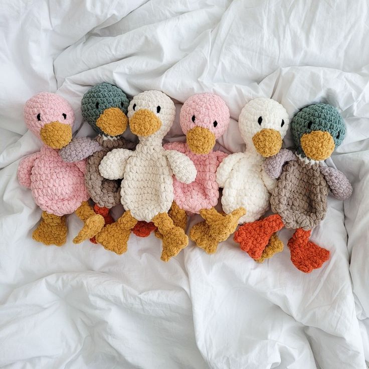 five crocheted stuffed ducks are lined up on a bed sheet with white sheets