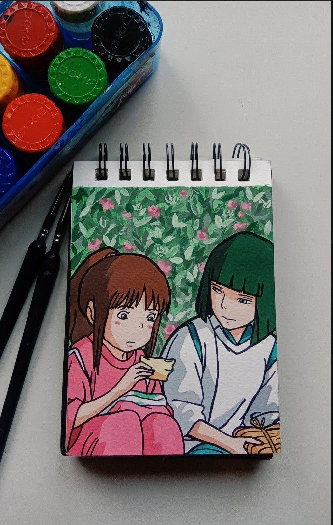 a notebook with an image of two anime characters on it next to paintbrushes