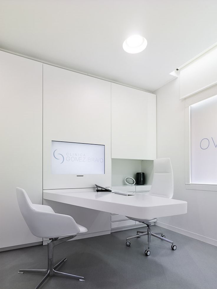 a white desk and chair in an office space with large windows on the wall behind it