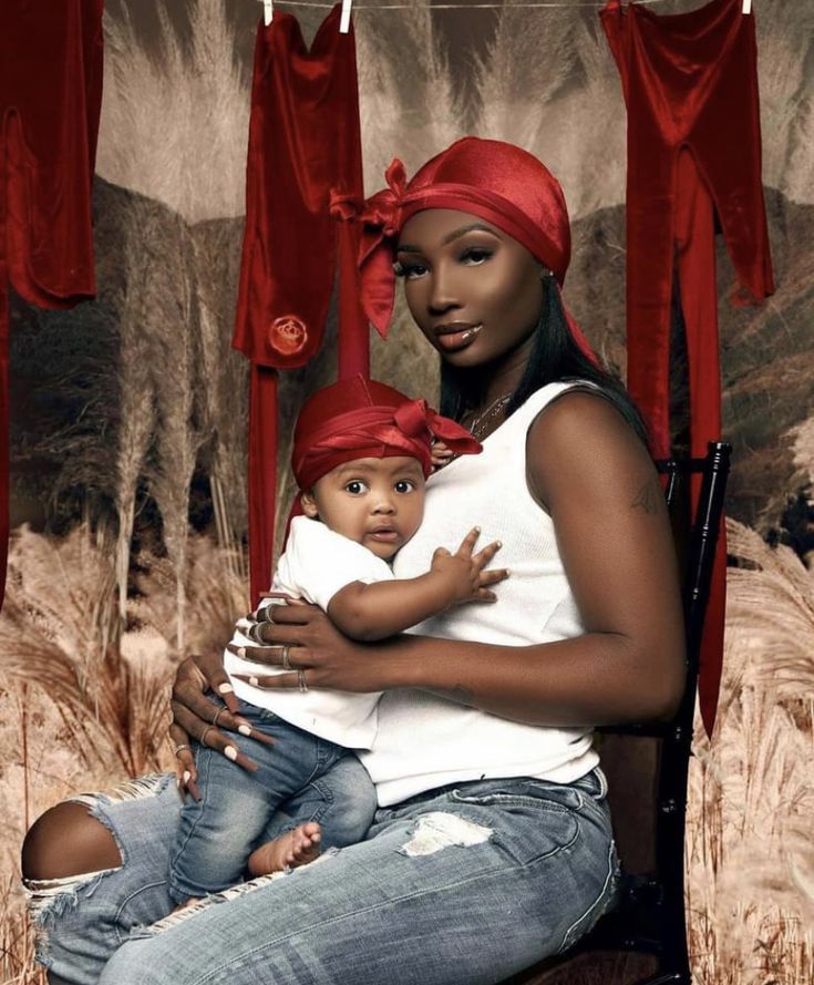 a woman holding a small child in her lap while sitting on a chair with red drapes hanging from the ceiling