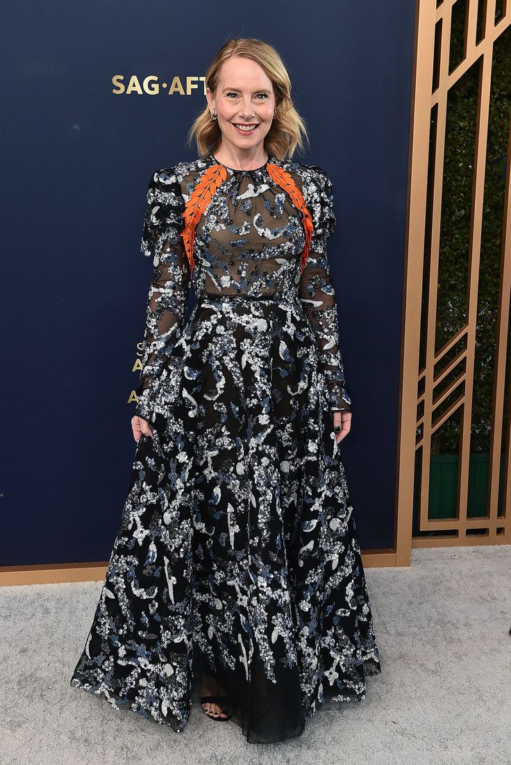 a woman in a black and white dress standing on a carpet with an orange ribbon around her neck