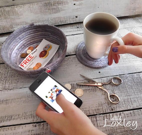 a person holding a smart phone next to a cup of coffee and scissors on a wooden table