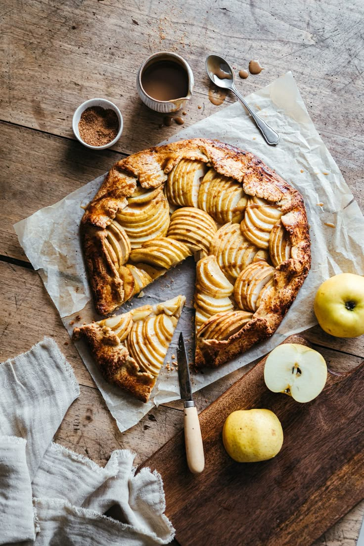 an apple pie with one slice cut out and some apples on the table next to it