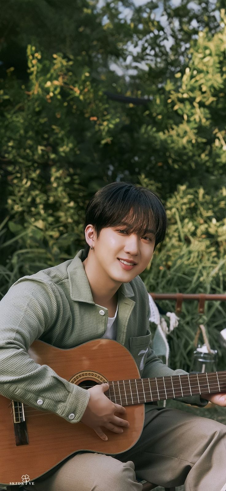 a young man is playing an acoustic guitar in front of some bushes and trees,