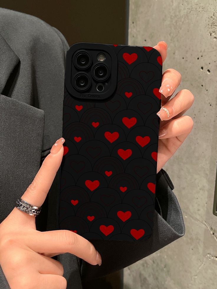 a woman holding up her phone case with red hearts on black paper in front of her