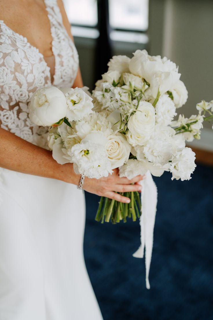 a woman in a wedding dress holding a bridal bouquet with white flowers on it