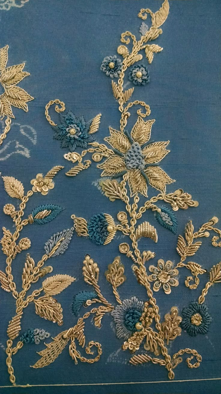 an embroidered blue cloth with gold flowers and leaves on the side, in front of a white background