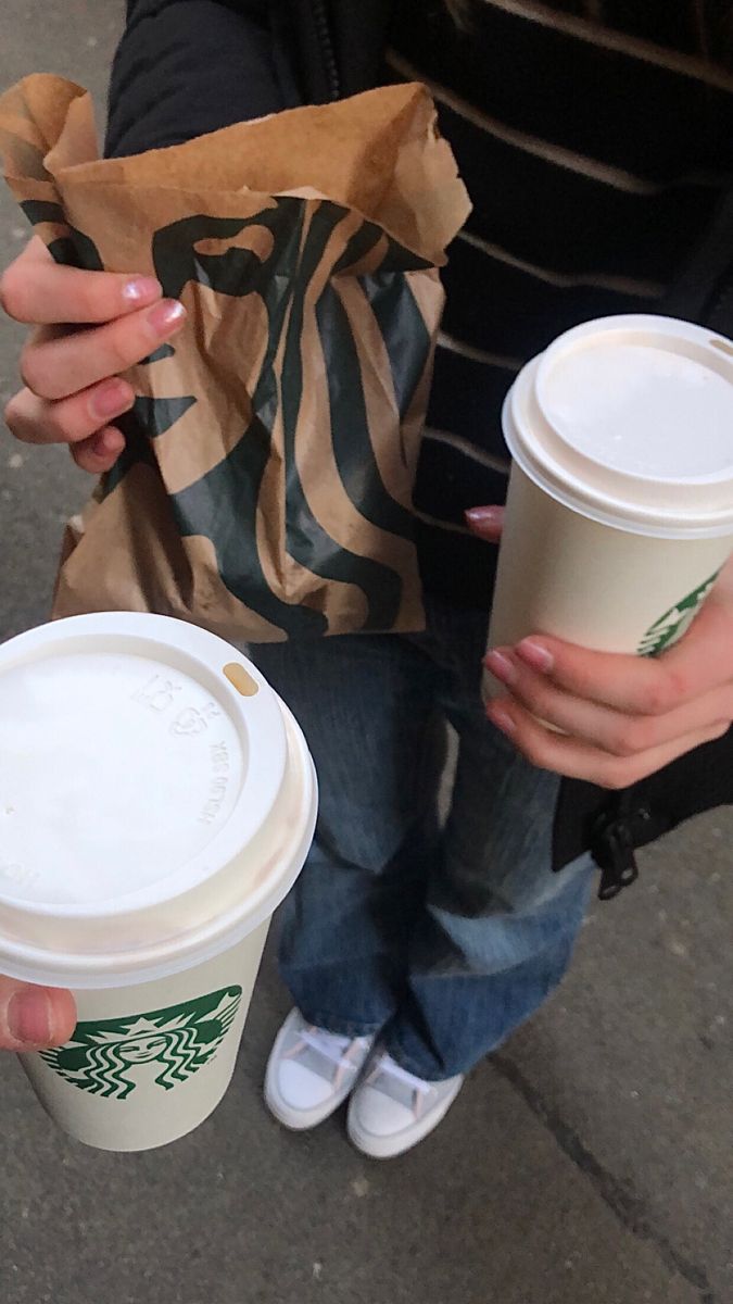 two people holding coffee cups in their hands while sitting on the ground next to each other