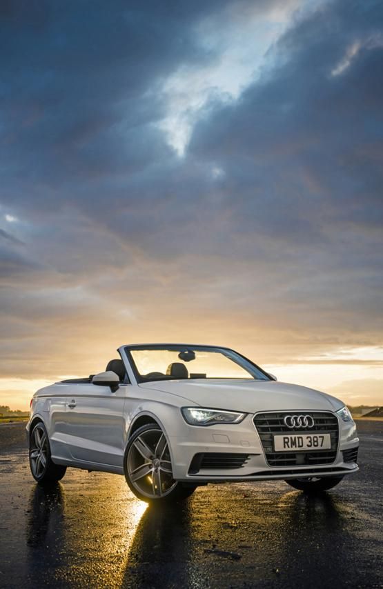 a white convertible car parked on top of a parking lot next to a cloudy sky