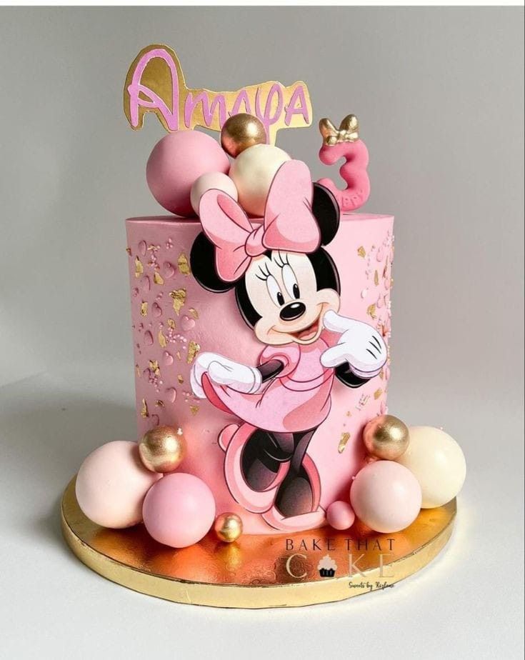 a pink and gold minnie mouse birthday cake on a stand with decorations around it,