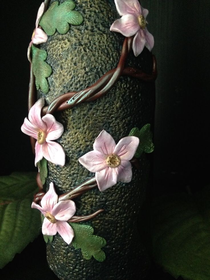 a green vase with pink flowers on it's side and leaves around the base