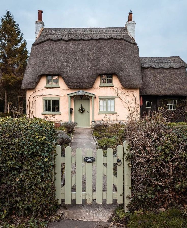 a white house with a thatched roof and green hedges around it's front door