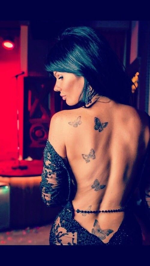 a woman with tattoos on her back and butterfly tattoo on her lower back, standing in front of a couch