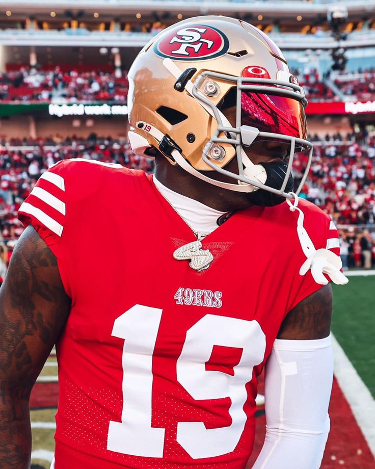 a football player wearing a helmet on the sidelines at a game with fans in the stands