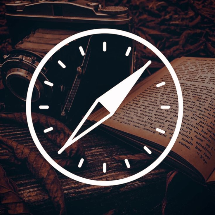 an open book sitting on top of a wooden table next to a clock and a compass