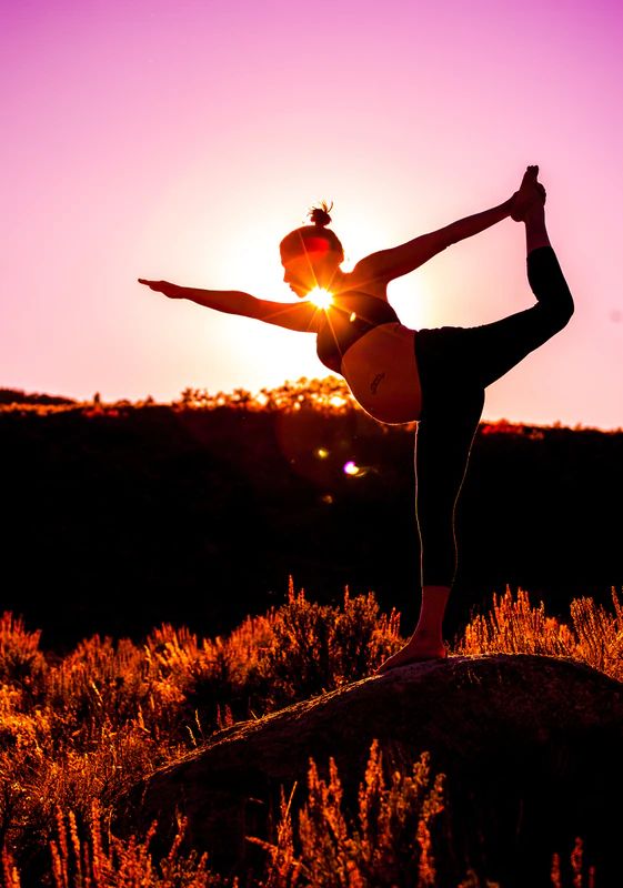 a woman doing yoga on top of a rock in front of the sun at sunset