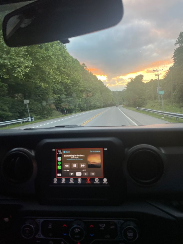 the dashboard of a vehicle on a road with trees in the background and an orange sky