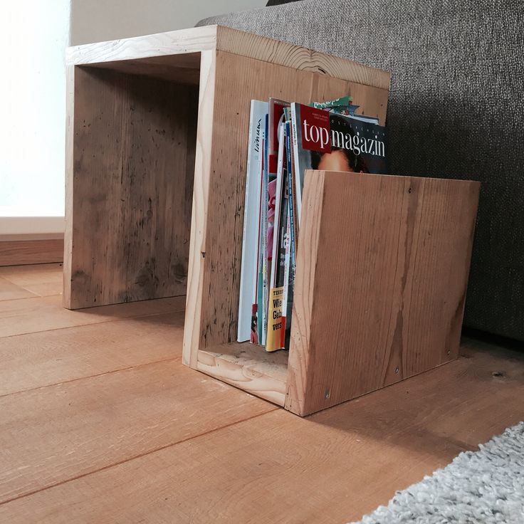 a wooden book holder with magazines in it sitting on the floor next to a couch