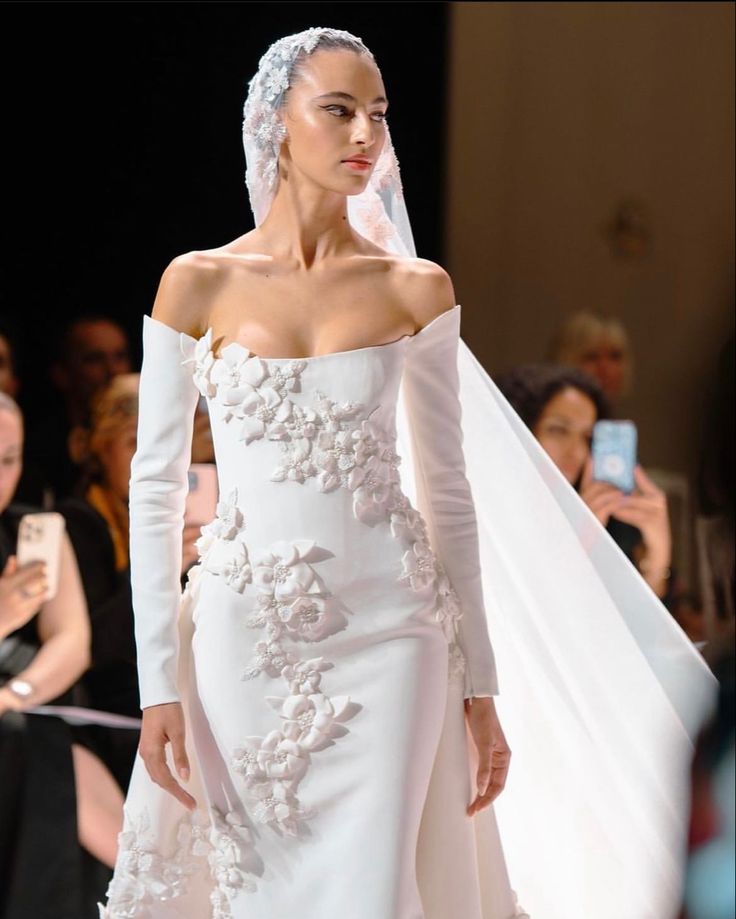 a model walks down the runway in a white wedding dress with flowers on her veil