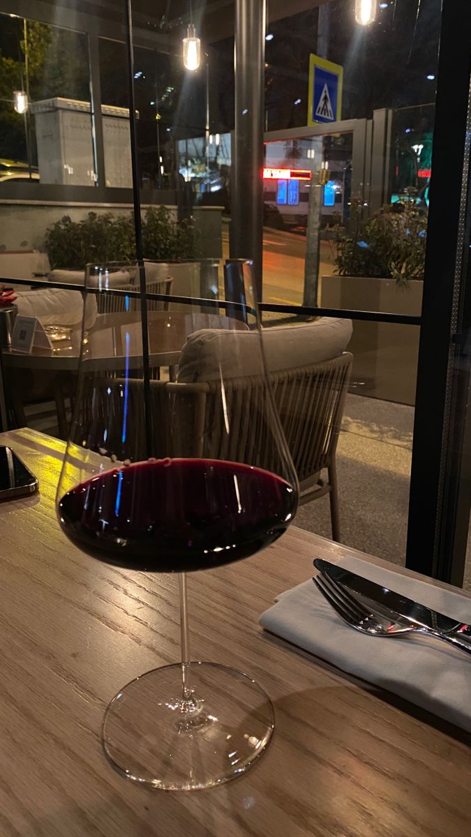 a glass of wine sitting on top of a wooden table next to a knife and fork