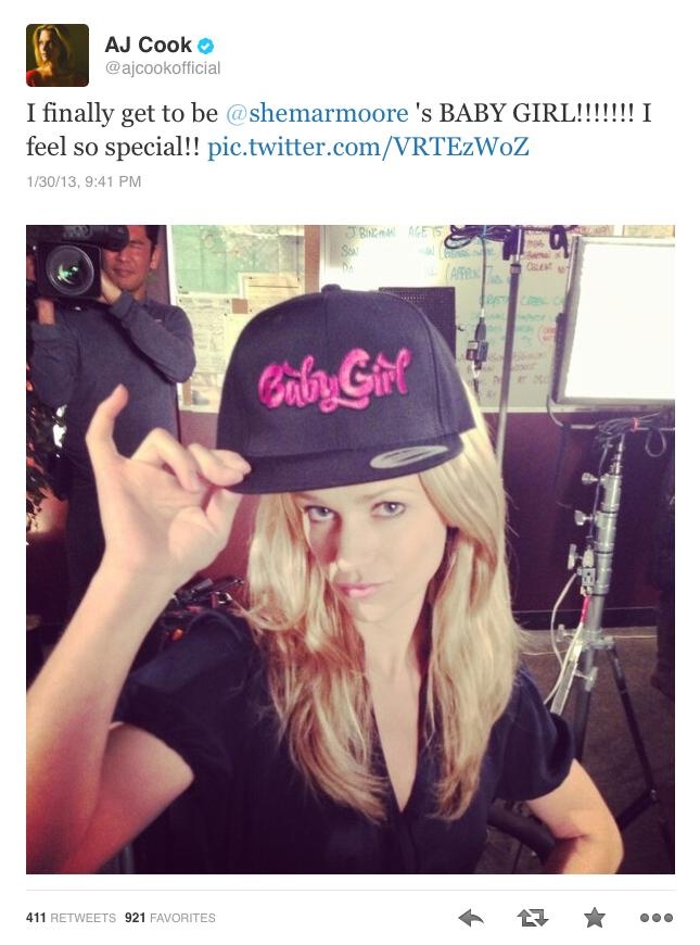 a woman wearing a black hat and making the peace sign with her hand while sitting in front of a camera