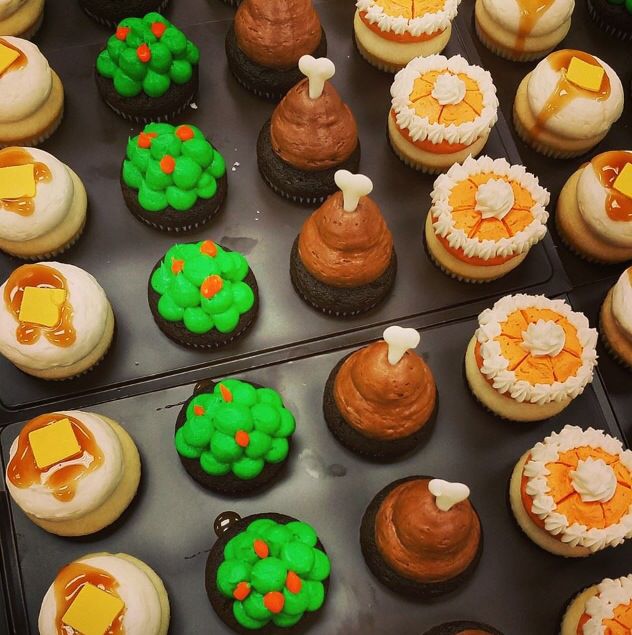 many cupcakes are decorated with orange, green and yellow icing on black trays