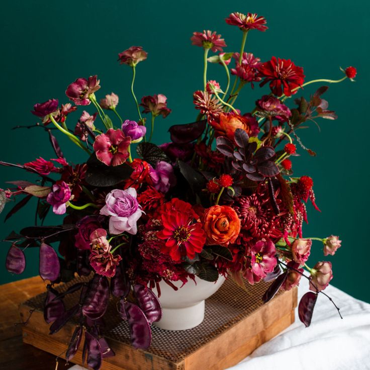 a white vase filled with lots of flowers on top of a wooden table next to a green wall