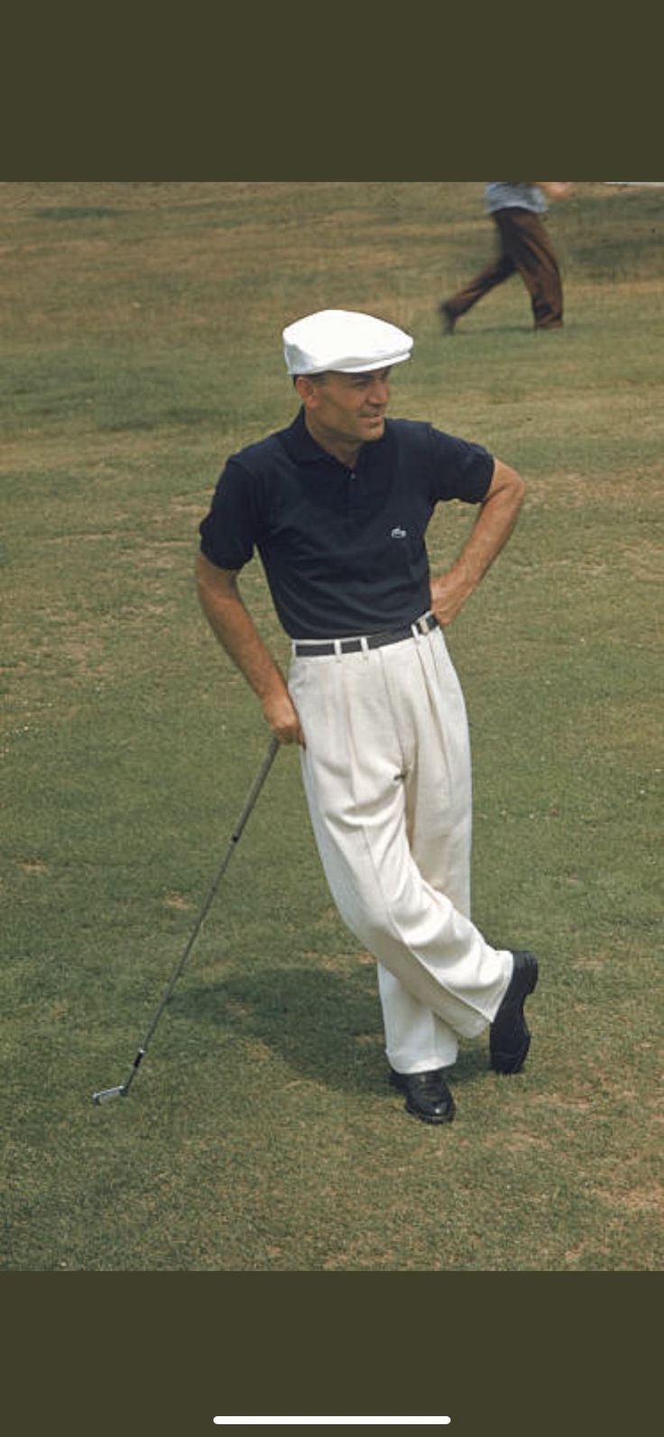 a man in white pants and a black shirt is standing on the grass with a golf club